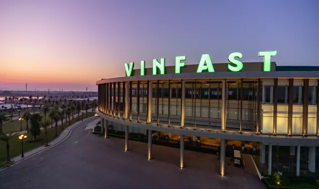 Gedung besar dengan tulisan VINFAST berwarna hijau menyala saat matahari terbenam.