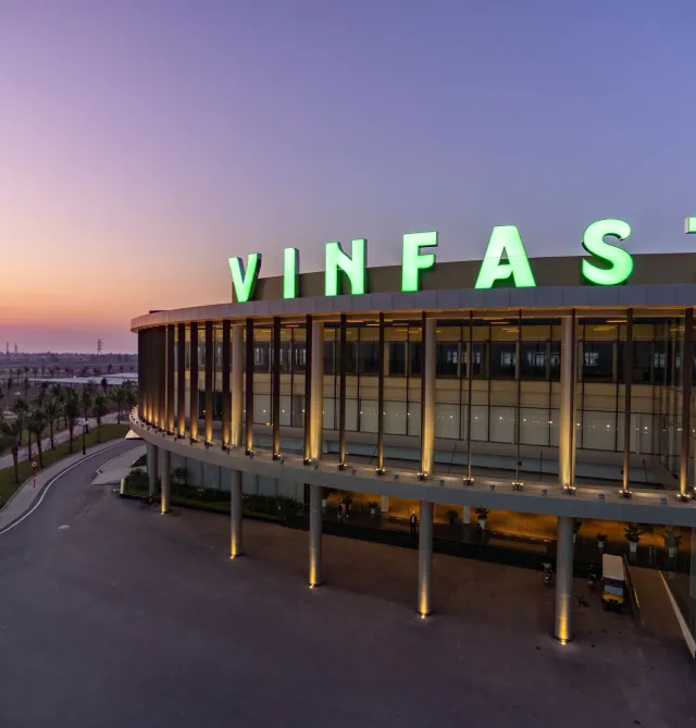 Tampak depan gedung dengan logo VINFAST hijau yang menyala di bawah langit senja.